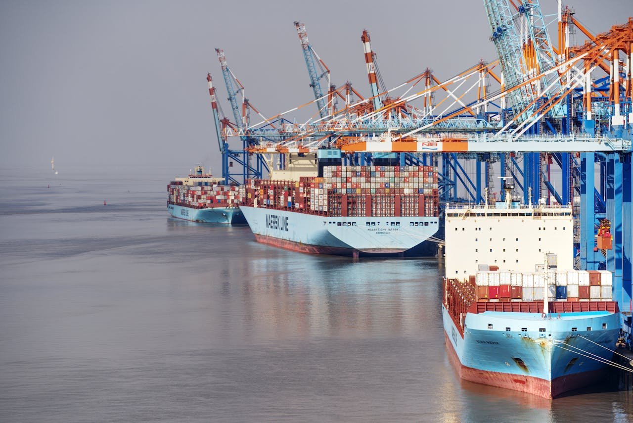 why-choose-us Container ships docked at a busy port with vibrant cranes and clear skies.